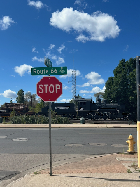 A Route 66 street sign in front of a black steam locomotive in Flagstaff