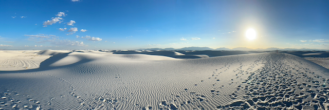 A panoramic view of white dunes, footprints, distant mountains, and the lowering sun