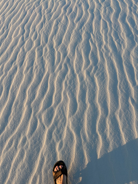 A sandal and long shadow over fine ripples in the white sand